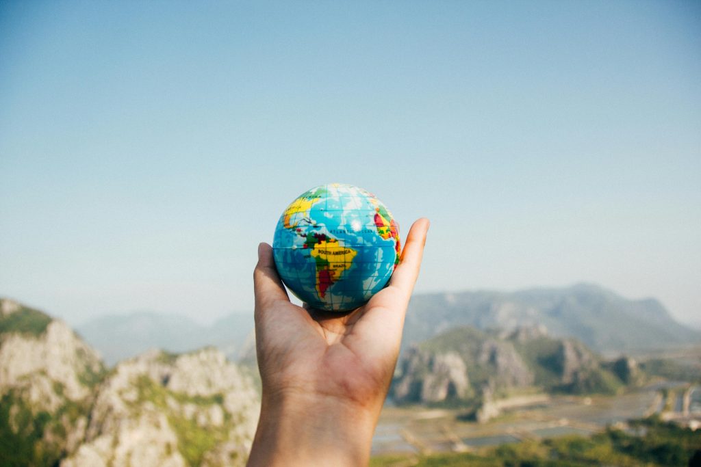 Hand holding a globe with a view of mountains in the background.